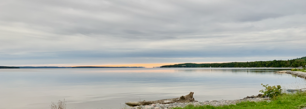 Shoreline in Temiskaming Shores with a grey sky and a little orange showing over the horizon.
